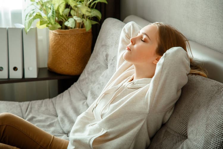 Mindfulness Meditation, young woman relaxed and leaning back on couch with her eyes closed - mindfulness meditation