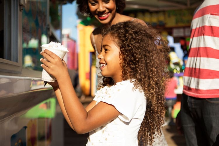 beautiful little Black girl with long hair getting ice cream at a summer carnival with her parents