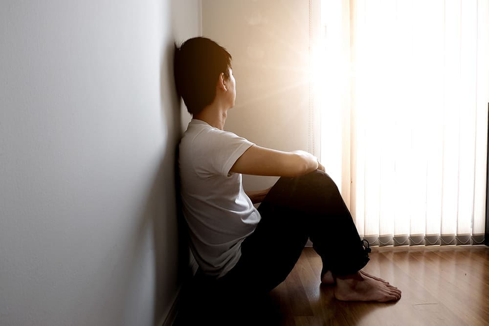 young teenager sitting in isolation up against a wall.